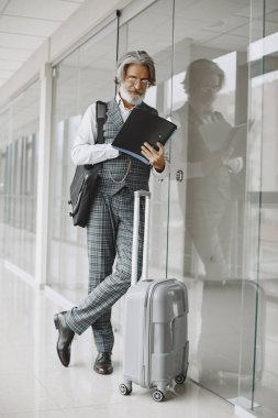 Havaalanında seyahat çantası taşıyan kıdemli işadamı.