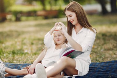 Anne ve küçük kızı bir ekose üzerinde oturup kitabı okuyorlar.