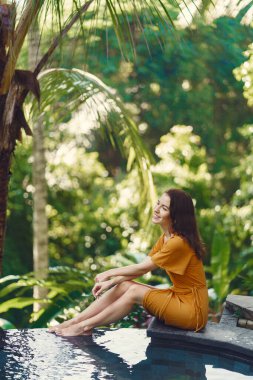 Sarı elbiseli kadın Bali 'de havuz kenarında oturuyor.