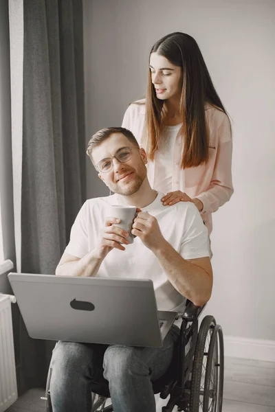 Joven en silla de ruedas usando laptop y novia abrazándolo en casa —  Fotos de Stock