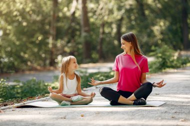 Anne ve kızı yaz parkında yoga yapıyor.