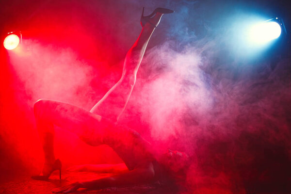 Girl with perfect slim body. Woman posing in bodysuit in red light in the smoke. Fashion studio shot.