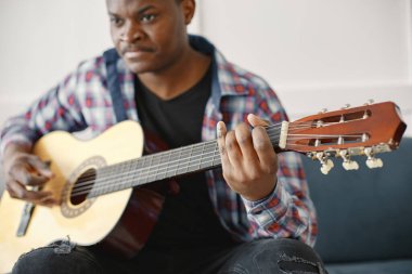 Kanepede oturan Afrikalı adam gitar çalıyor.
