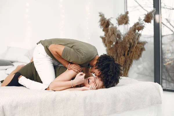 Multietniskt par kramas och kyssas på vit säng — Stockfoto