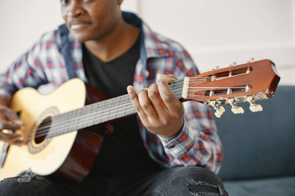 African man playing guitar while sitting on sofa