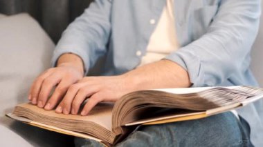 Kör genç adam kanepede kabartma kitap okuyor.