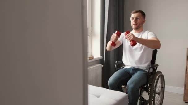 Молодой человек в инвалидной коляске делает упражнения в помещении — стоковое видео