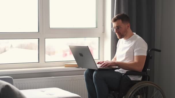Junger Mann im Rollstuhl arbeitet zu Hause mit Laptop — Stockvideo