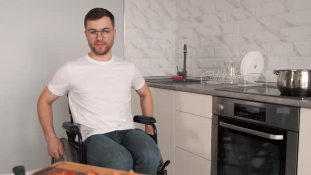 Молодой человек-инвалид в инвалидном кресле готовит еду на кухне — стоковое видео