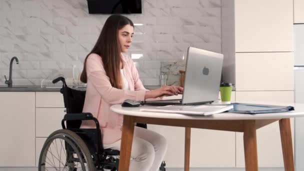 Jonge gehandicapte vrouw in rolstoel die thuis met laptop en tablet werkt — Stockvideo