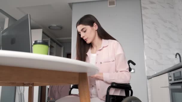 Mladá zdravotně postižená žena na invalidním vozíku pracuje s notebookem a tabletem doma — Stock video