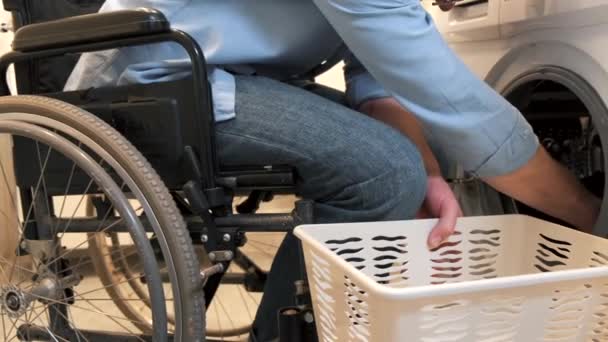 Homem deficiente em cadeira de rodas colocar roupa na máquina de lavar roupa — Vídeo de Stock