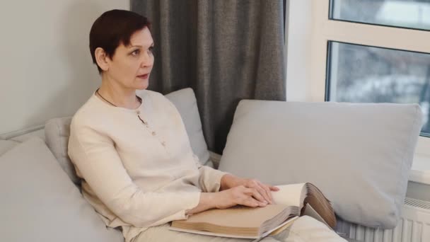 Madura mujer leer braille libro en sofá — Vídeo de stock