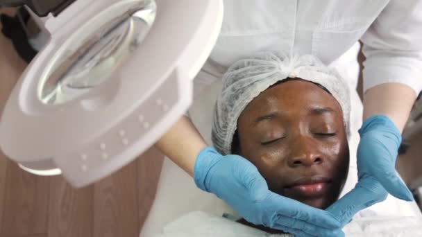 Cosmetólogo haciendo masaje facial manualmente al cliente africano — Vídeos de Stock