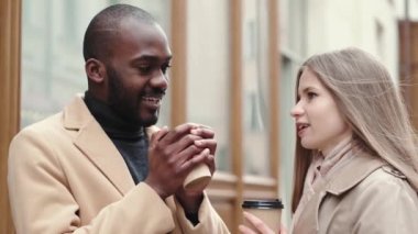 Afrika kökenli Amerikalı erkek ve Ukraynalı kadın şehirde yürümek için kahve içiyorlar.