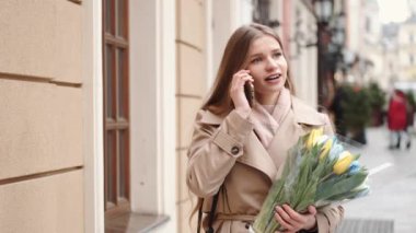 Halka açık bir yerde akıllı telefon kullanan bir sürü lale tutan güzel genç kadın.