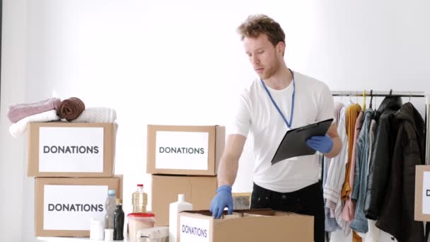 Jonge vrijwilliger die het donatievakje voor kleding controleert en aantekeningen maakt, humanitaire hulp — Stockvideo