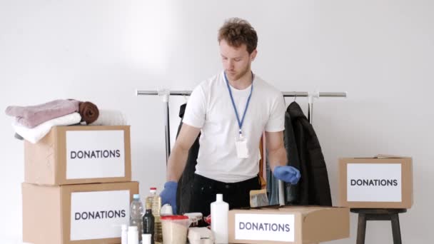Jonge vrijwilliger die het donatievakje voor kleding controleert en aantekeningen maakt, humanitaire hulp — Stockvideo