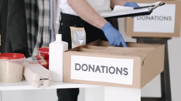 Jonge vrijwilliger die het donatievakje voor kleding controleert en aantekeningen maakt, humanitaire hulp — Stockvideo