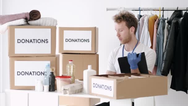 Jonge vrijwilliger die het donatievakje voor kleding controleert en aantekeningen maakt, humanitaire hulp — Stockvideo