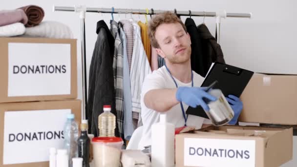 Jonge vrijwilliger die het donatievakje voor kleding controleert en aantekeningen maakt, humanitaire hulp — Stockvideo