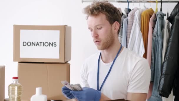 Genç gönüllü kıyafet bağış kutusunu kontrol ediyor ve not alıyor, insani yardım — Stok video