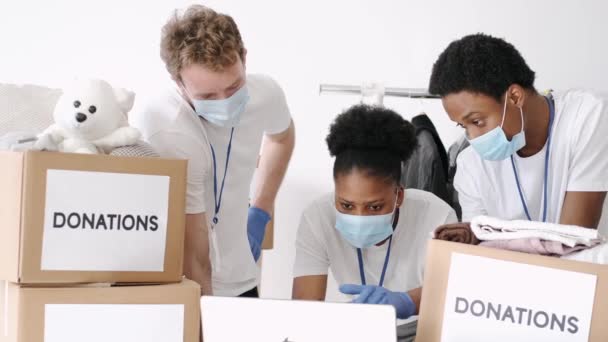 Voluntarios con máscaras clasificando donaciones de ropa durante pandemia — Vídeo de stock