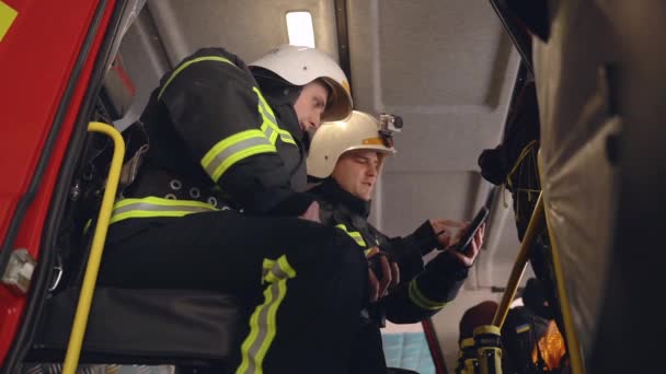 Dua petugas pemadam kebakaran menganalisis data yang melihat pada tablet digital di kabin truk — Stok Video