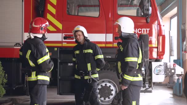 Tres equipos de bomberos de pie en el camión de bomberos en la estación — Vídeo de stock