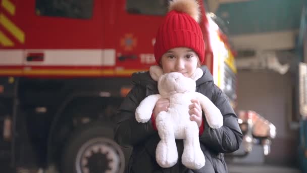 Niña sosteniendo un juguete de pie en una estación de bomberos — Vídeos de Stock