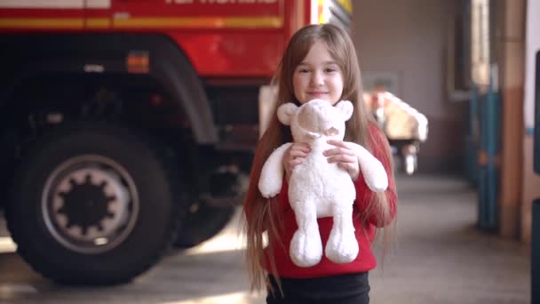 Niña sosteniendo un juguete de pie en una estación de bomberos — Vídeo de stock