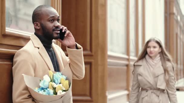 Çiçekleri olan, telefonla konuşan ve kız arkadaşını bekleyen Afrikalı Amerikalı bir adam. — Stok video