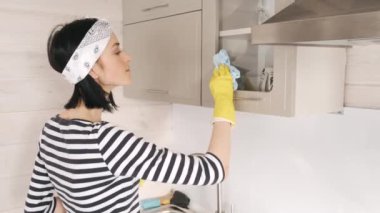 Genç bir kadın mutfakta dolapları yıkıyor.