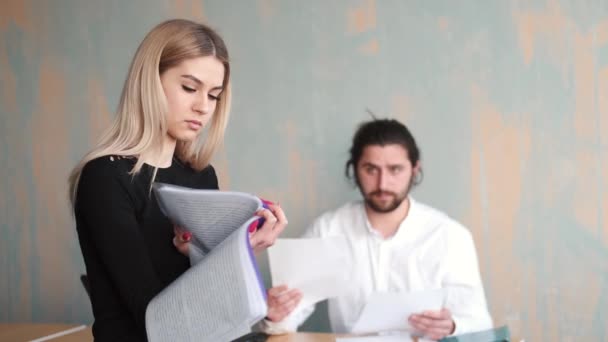 Young woman office worker close up work with papers and her male collegue at the background — Stock Video