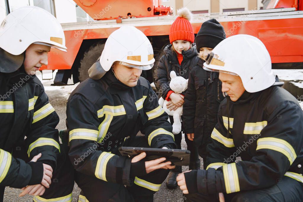 Male firefighters show children on a tablet safety rules