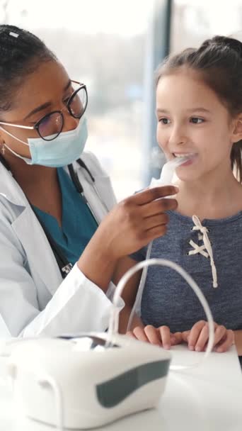 Mujer africana médico sostiene un inhalador de vapor máscara para niña — Vídeos de Stock