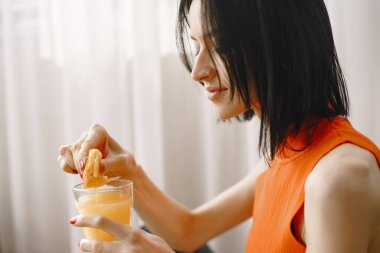 Turuncu ceketli kız yere oturup meyve suyu içiyor.