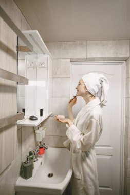 Beyaz önlüklü ve havlulu bir kız banyo yaparken yüzüne bakar.