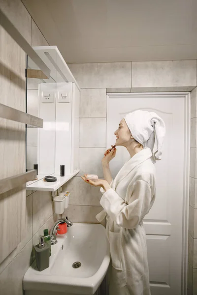 Beyaz önlüklü ve havlulu bir kız banyo yaparken yüzüne bakar. — Stok fotoğraf
