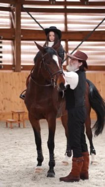 Senior man assisting granddaughter horseback riding in ranch