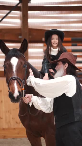 Senior man assisting granddaughter horseback riding in ranch — Stock video