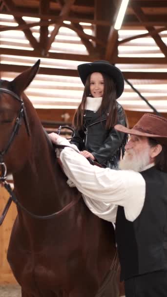 Senior man assisting granddaughter horseback riding in ranch — Stockvideo