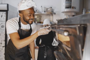 Afro-Amerikalı adam ticari mutfakta pizza pişiriyor.