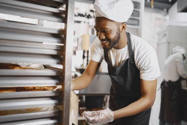 Afroamerikanischer Bäcker in Uniform sortiert Backwaren auf Paletten — Stockfoto