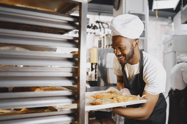 Afroamerikanischer Bäcker in Uniform sortiert Backwaren auf Paletten — Stockfoto