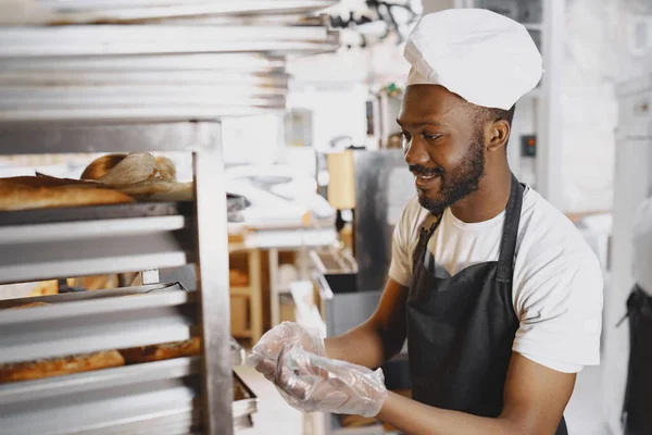 Afroamerikanischer Bäcker in Uniform sortiert Backwaren auf Paletten — Stockfoto