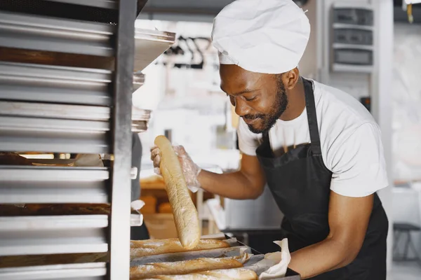 Afroamerikanischer Bäcker in Uniform sortiert Backwaren auf Paletten — Stockfoto