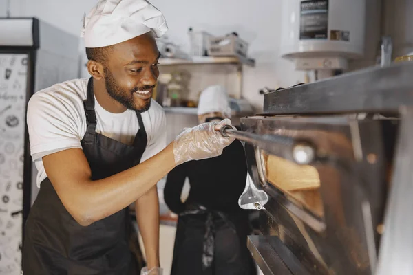 Hombre africano mericano horneando pizza en la cocina comercial —  Fotos de Stock