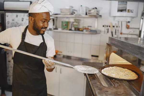 Afrikanischer Mann backt Pizza in Großküche — Stockfoto