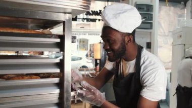 Üniformalı Afrikalı Amerikalı fırıncı paletler üzerinde fırınlanmış ürünleri sıralıyor